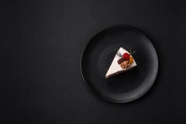Delicious beautiful piece of cake with cream and berries on a black ceramic plate on a dark concrete background