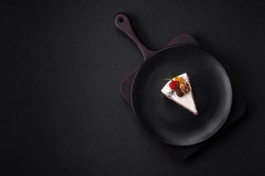 Delicious beautiful piece of cake with cream and berries on a black ceramic plate on a dark concrete background