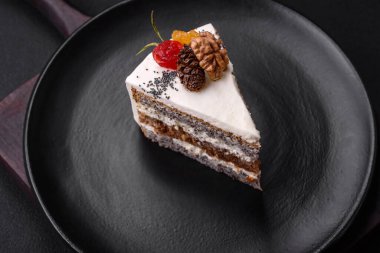 Delicious beautiful piece of cake with cream and berries on a black ceramic plate on a dark concrete background