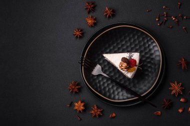 Delicious beautiful piece of cake with cream and berries on a black ceramic plate on a dark concrete background