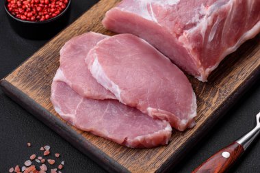 Tahta kesme tahtasındaki taze, sulu domuz eti. Baharatlar ve koyu beton arka planda tuz.