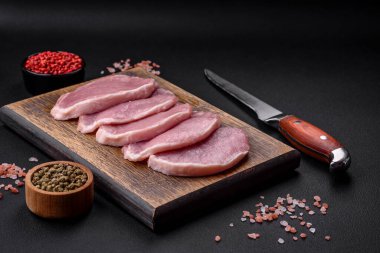 Tahta kesme tahtasındaki taze, sulu domuz eti. Baharatlar ve koyu beton arka planda tuz.