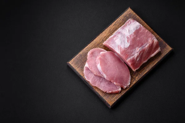 濃いコンクリートの背景にスパイスと塩で木製のまな板の上に新鮮なジューシーな豚肉 — ストック写真