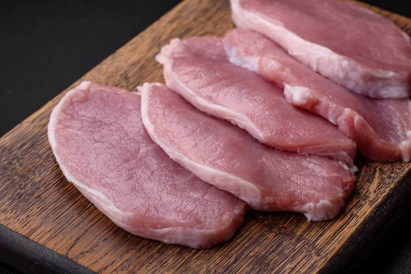 stock image Fresh juicy pork on a wooden cutting board with spices and salt on a dark concrete background