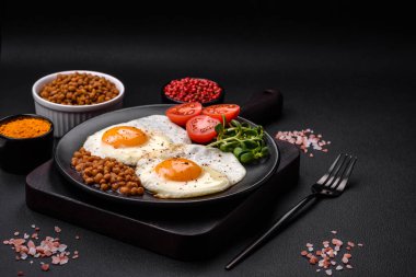 İki sahanda yumurta, konserve mercimek, çimento ve baharatlı mikro yeşillikler ve koyu beton bir arka plandan oluşan lezzetli ve doyurucu bir kahvaltı.