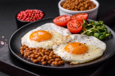 İki sahanda yumurta, konserve mercimek, çimento ve baharatlı mikro yeşillikler ve koyu beton bir arka plandan oluşan lezzetli ve doyurucu bir kahvaltı.