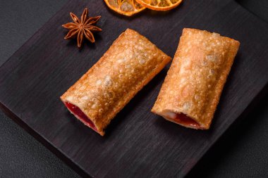 Tahta kesme tahtasının üzerinde kiraz reçelli lezzetli çıtır turta, koyu beton arka planda.