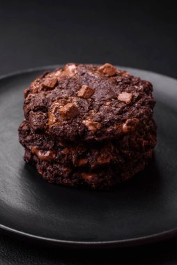 Lezzetli taze yulaf ezmesi yuvarlak kurabiyeler, siyah seramik tabakta çikolata, koyu beton arka planda.