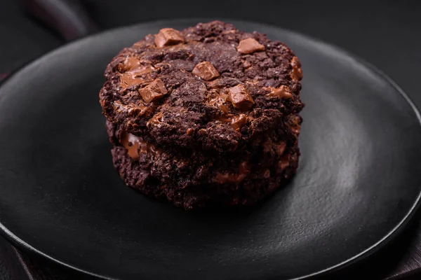 stock image Delicious fresh oatmeal round cookies with chocolate on a black ceramic plate on a dark concrete background