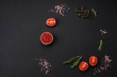 Biberiye, kekik, tüm baharatlar, tuz, kiraz domatesleri ve diğer baharatlar koyu beton arka planda. Evde yemek pişirmek için malzemeler.