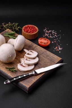 Tahta kesme tahtasındaki taze çiğ şampiyon mantarları koyu beton arka planda baharatlar ve otlarla.