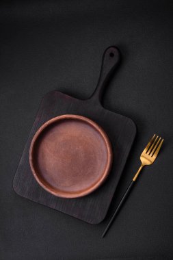 Koyu desenli beton arka planda boş kahverengi seramik plaka. Mutfak aletleri