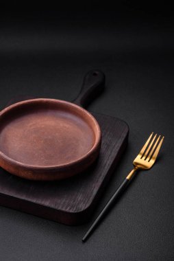 Koyu desenli beton arka planda boş kahverengi seramik plaka. Mutfak aletleri