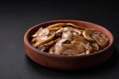 Kavrulmuş ya da pişirilmiş şampiyon mantarı. Kahverengi seramik tabakta soğan dilimleri ve koyu beton arka planda.