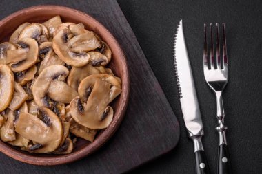 Kavrulmuş ya da pişirilmiş şampiyon mantarı. Kahverengi seramik tabakta soğan dilimleri ve koyu beton arka planda.