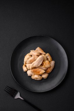 Yuvarlak bir seramik tabakta koyu beton arka planda baharat ve otlarla pişirilmiş lezzetli tavuk dilimleri.