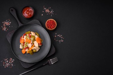 Lezzetli tavuk dilimleri ve buğulanmış sebzeler havuç, brokoli, kuşkonmaz fasulyesi ve biber koyu beton arka planda.