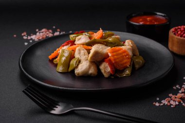 Lezzetli tavuk dilimleri ve buğulanmış sebzeler havuç, brokoli, kuşkonmaz fasulyesi ve biber koyu beton arka planda.