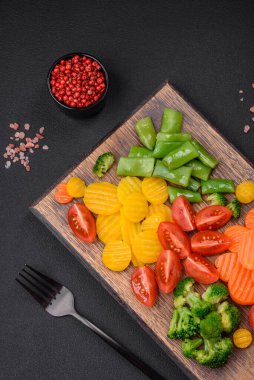 Taze ve buğulanmış sebze salatası kiraz domatesleri, brokoli, havuç ve kuşkonmaz fasulyeleri koyu beton arka planda.