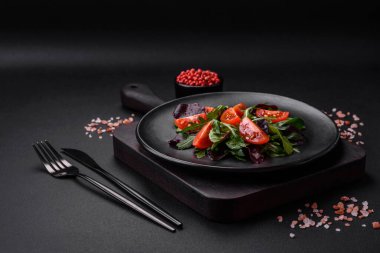 Taze vişneli domates salatası, roka, ıspanak, taze pancar yaprakları ve koyu beton arka planda diğer yeşiller.