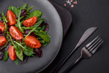 Taze vişneli domates salatası, roka, ıspanak, taze pancar yaprakları ve koyu beton arka planda diğer yeşiller.