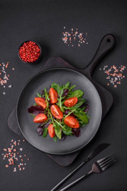 Taze vişneli domates salatası, roka, ıspanak, taze pancar yaprakları ve koyu beton arka planda diğer yeşiller.