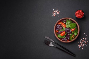 Taze vişneli domates salatası, roka, ıspanak, taze pancar yaprakları ve koyu beton arka planda diğer yeşiller.