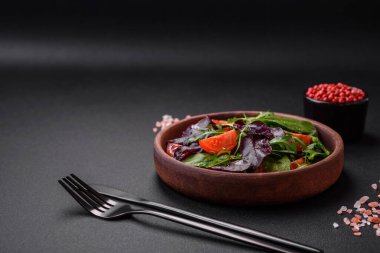 Taze vişneli domates salatası, roka, ıspanak, taze pancar yaprakları ve koyu beton arka planda diğer yeşiller.