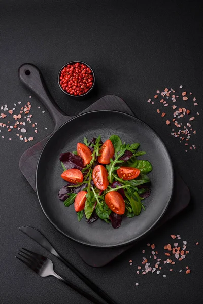 stock image Salad of fresh cherry tomatoes, arugula, spinach, young beet leaves and other greens on a dark concrete background