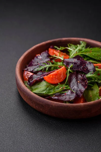 Taze vişneli domates salatası, roka, ıspanak, taze pancar yaprakları ve koyu beton arka planda diğer yeşiller.