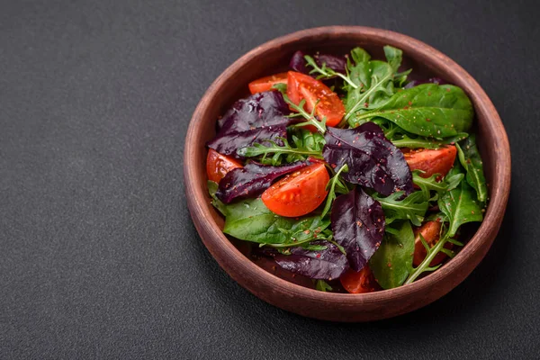 Taze vişneli domates salatası, roka, ıspanak, taze pancar yaprakları ve koyu beton arka planda diğer yeşiller.