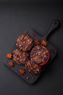 Koyu beton arka planda siyah seramik tabakta çikolatalı ve fındıklı lezzetli çıtır yulaf ezmeli kurabiyeler.