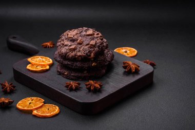 Koyu beton arka planda siyah seramik tabakta çikolatalı ve fındıklı lezzetli çıtır yulaf ezmeli kurabiyeler.