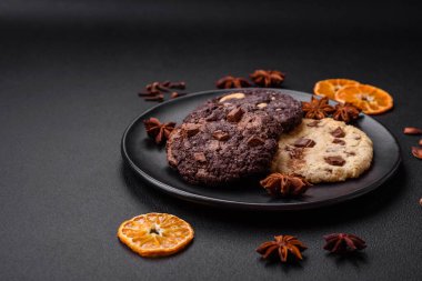 Koyu beton arka planda siyah seramik tabakta çikolatalı ve fındıklı lezzetli çıtır yulaf ezmeli kurabiyeler.