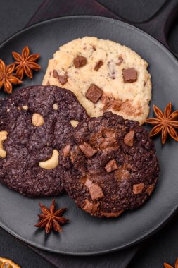 Koyu beton arka planda siyah seramik tabakta çikolatalı ve fındıklı lezzetli çıtır yulaf ezmeli kurabiyeler.