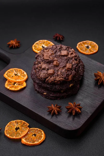 stock image Delicious fresh crispy oatmeal cookies with chocolate and nuts on a black ceramic plate on a dark concrete background