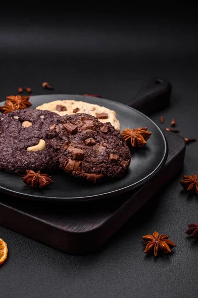 stock image Delicious fresh crispy oatmeal cookies with chocolate and nuts on a black ceramic plate on a dark concrete background