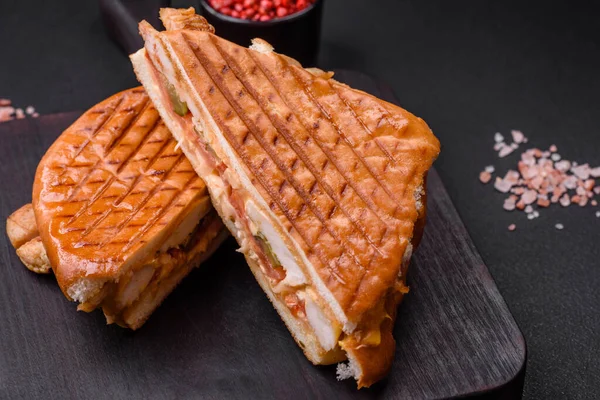 stock image Delicious crispy sandwich with chicken breast, tomatoes, ketchup and spices on a dark concrete background