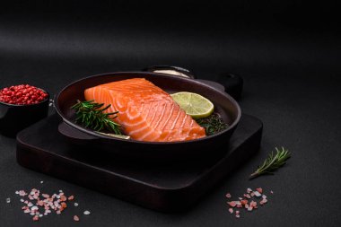 Koyu beton arka planda baharat ve bitkilerle taze çiğ balık filetosu.