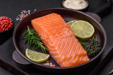 Koyu beton arka planda baharat ve bitkilerle taze çiğ balık filetosu.