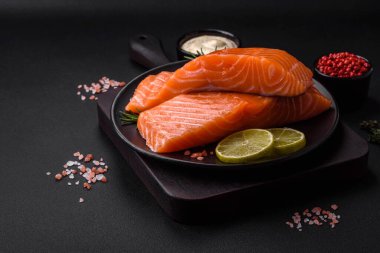 Koyu beton arka planda baharat ve bitkilerle taze çiğ balık filetosu.