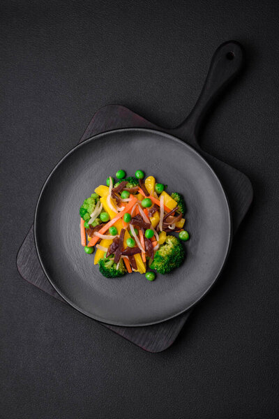 Delicious steamed vegetables broccoli, mushrooms, peas, carrots and onions on a dark concrete background