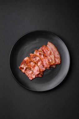 Lezzetli taze domuz pastırması şeritleri ve koyu beton arka planda baharatlar.