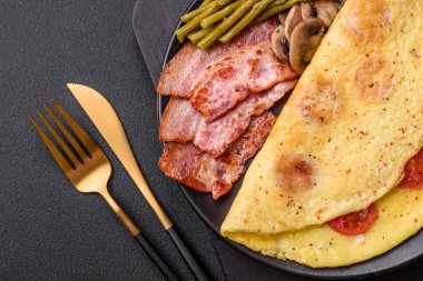 Çeri domatesli leziz taze omlet, pastırma, kuşkonmaz ve koyu beton arka planda baharatlar.