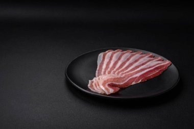 Tuz ve baharatlı leziz taze pancetta koyu beton arka planda ince dilimler halinde kesilmiş.