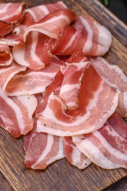 Tuz ve baharatlı leziz taze pancetta koyu beton arka planda ince dilimler halinde kesilmiş.