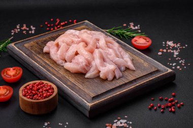 Çiğ tavuk filetosu, ahşap bir kesim tahtasının üzerinde baharat ve otlarla dilimlenmiş.