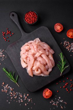 Çiğ tavuk filetosu, ahşap bir kesim tahtasının üzerinde baharat ve otlarla dilimlenmiş.