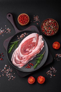 Baharat ve otlarla dilimlenmiş taze çiğ domuz pastırması ve koyu beton bir arka plan.