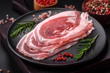 Baharat ve otlarla dilimlenmiş taze çiğ domuz pastırması ve koyu beton bir arka plan.